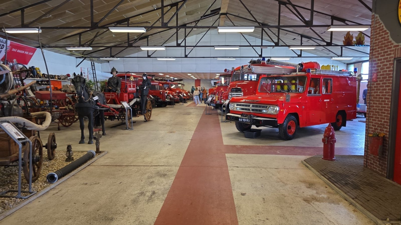 Interior view of a museum hall with red fire engines and a carriage.