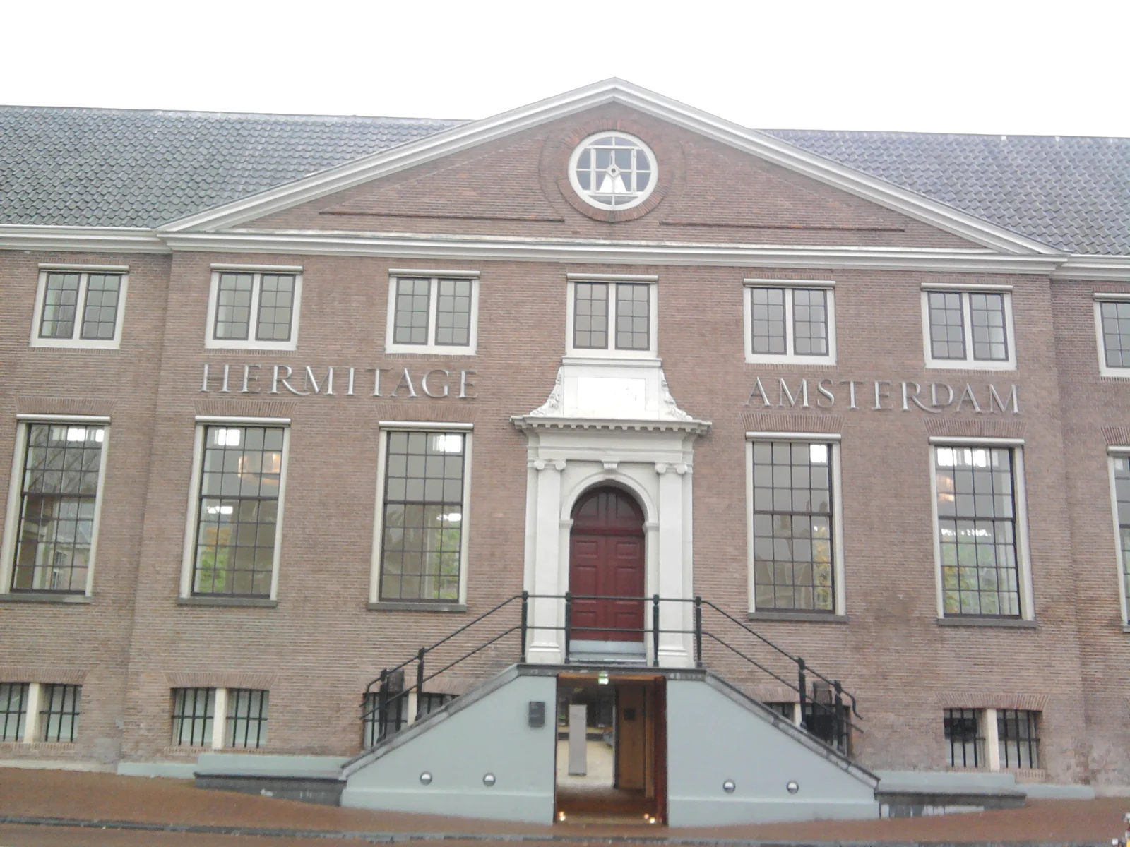 Museumseingang mit zwei Treppen, weißer Türumrahmung und dem Fassadenschriftzug Hermitage Amsterdam.