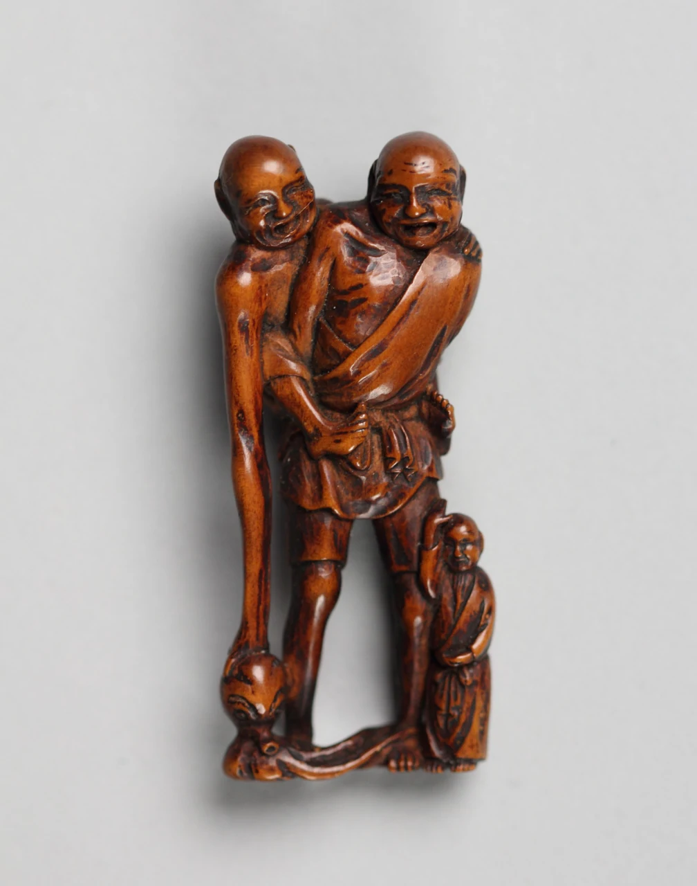 Een houten netsuke met twee langgerekte figuren, een kind en een octopus.