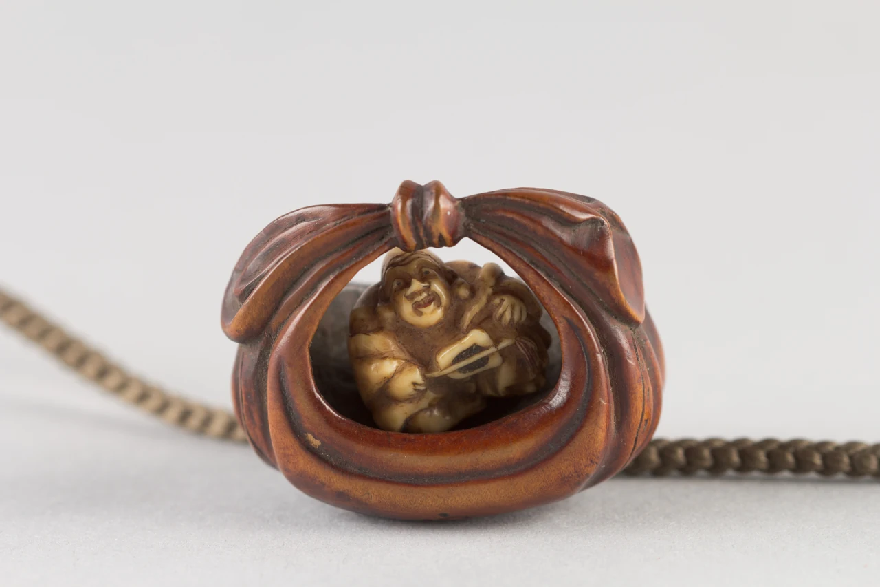 Een kleine netsuke in de vorm van een zak waaruit een figuur van Hotei verschijnt.