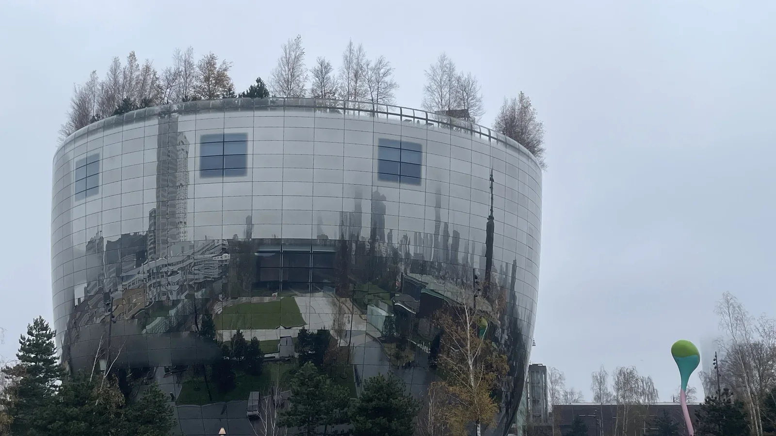 Het ronde, spiegelende Depot Boijmans Van Beuningen met bomen op het dak en weerspiegelingen van de stad.