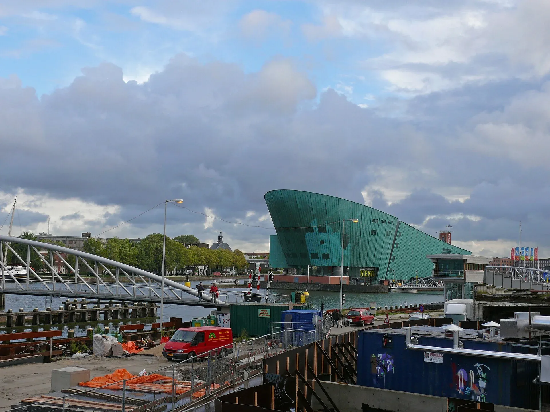 Groen gebouw van NEMO aan het water onder een bewolkte hemel.