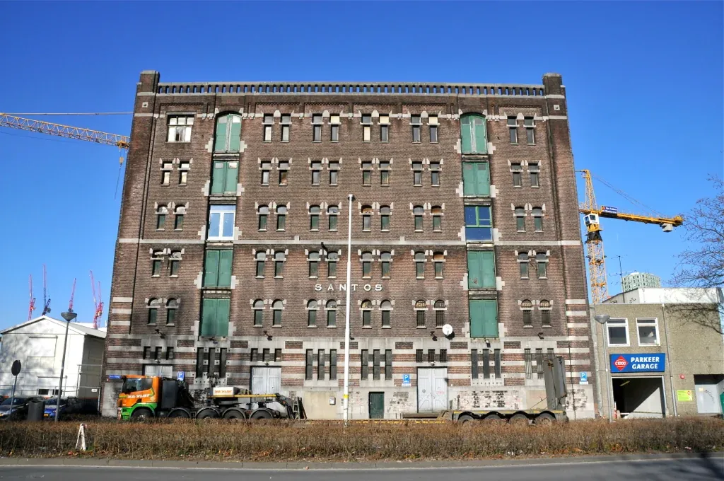 Backsteinfassade des Lagerhauses Santos in Rotterdam mit grünen Fensterläden unter blauem Himmel.