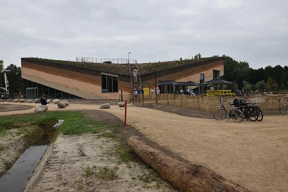 Nouveau bâtiment du musée avec toit végétalisé en pente, chemins, quelques visiteurs et travaux sur le terrain.
