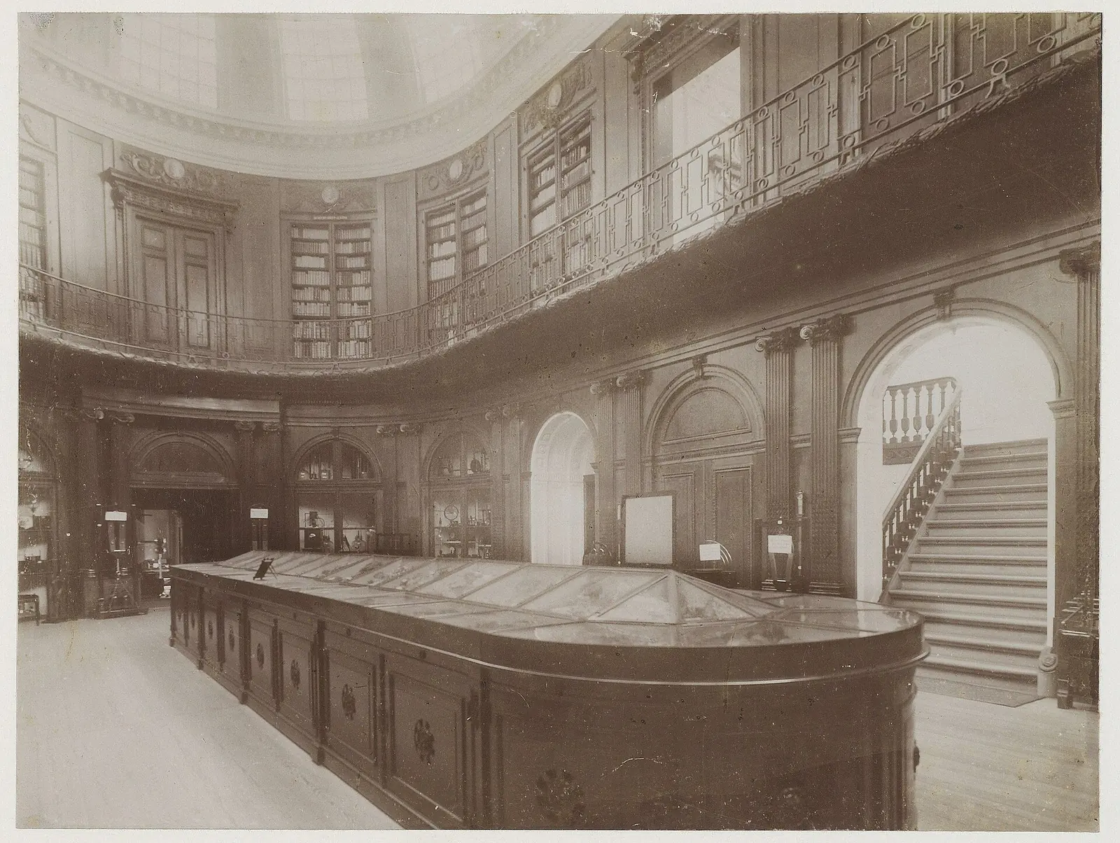 Historische zwart-witfoto van de Ovale Zaal met grote centrale vitrine en boeken op de omloop.