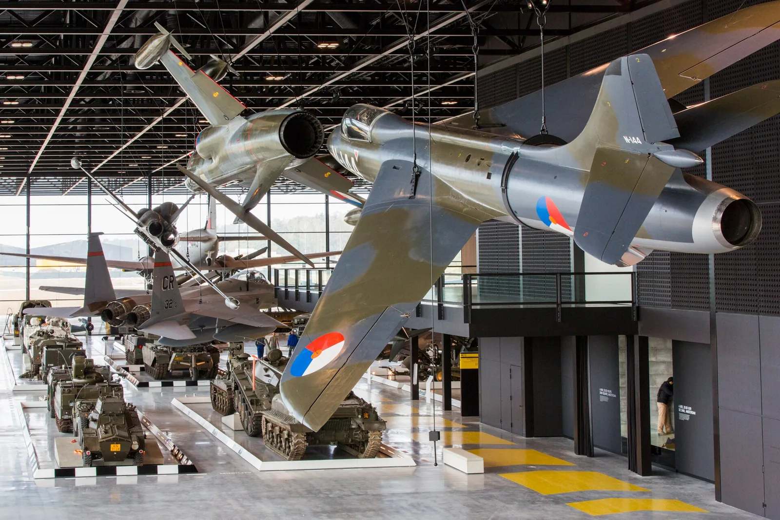 Vliegtuigen hangen boven rijen militaire voertuigen in de grote hal van het Arsenaal.