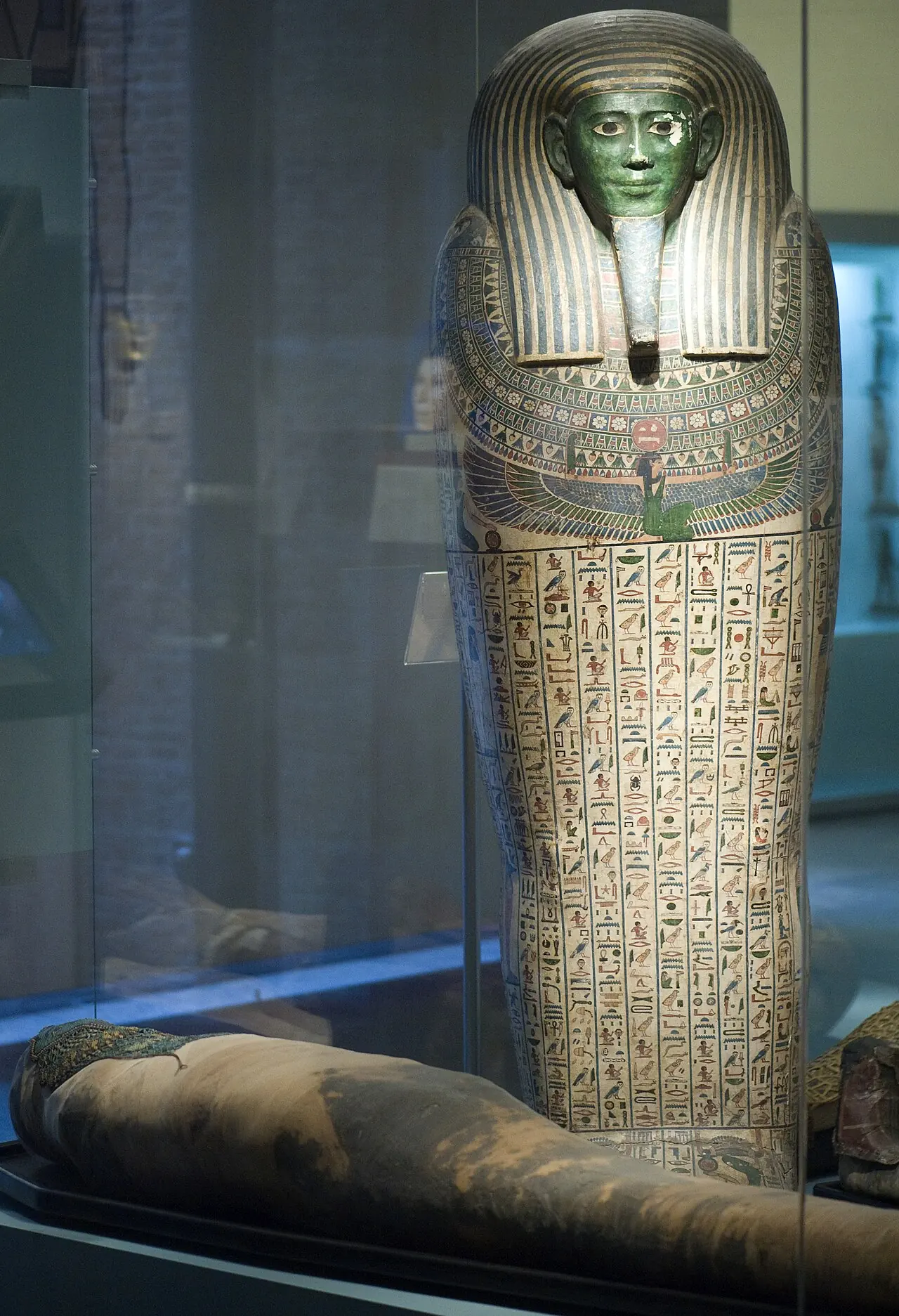 Beschilderde Egyptische mummiekist met hiërogliefen, naast een in linnen gewikkeld lichaam.