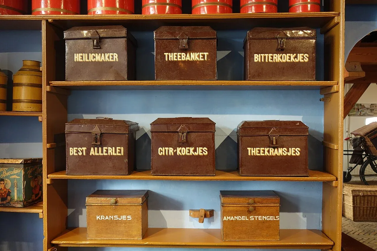 Houten schappen met oude, gelabelde koekblikken in het Bakkerijmuseum.