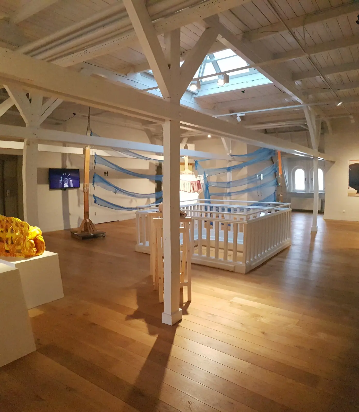 Museumssaal unter Holzbalken und Dachlicht mit einer Ausstellung von 2022.
