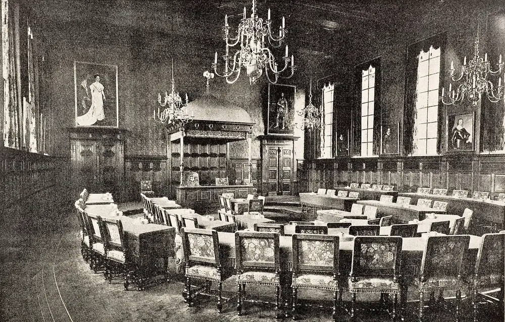 Zwart-witfoto van een historische Statenzaal met kroonluchters, tafels en stoelen.