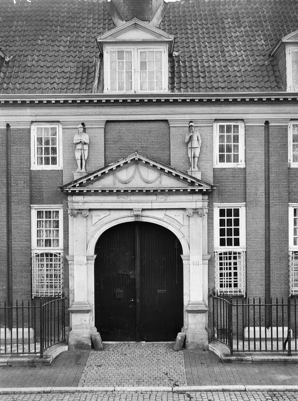 Historic black-and-white photograph of a stone entrance gate with pediment and two statues.